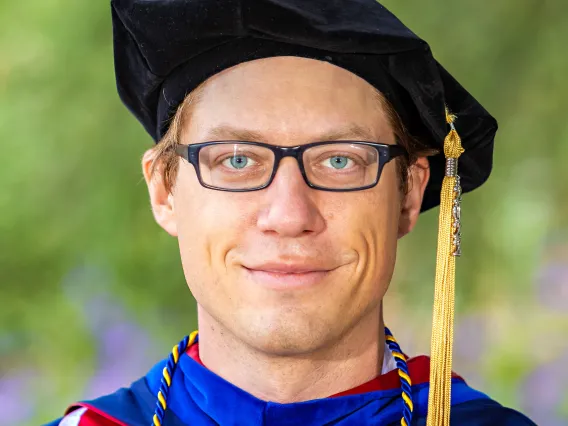 Image of man in graduation regalia smiling at camera