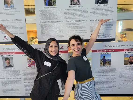 Two women arms out in front of poster