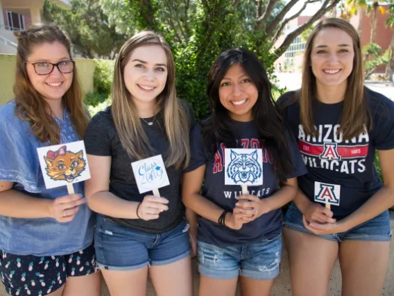 Four women holding up UArizona logos