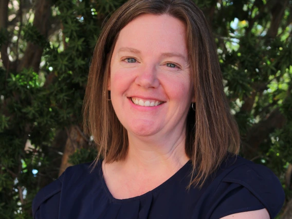 Image of woman smiling at camera with foliage in background