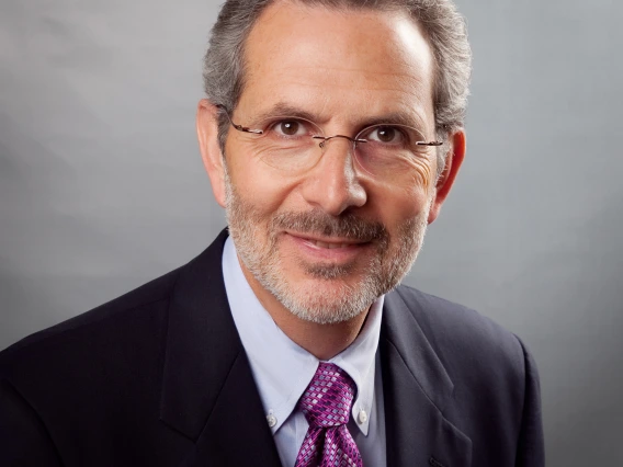 Headshot of man wearing suit with purple patterned tie and glasses smiling at the camera