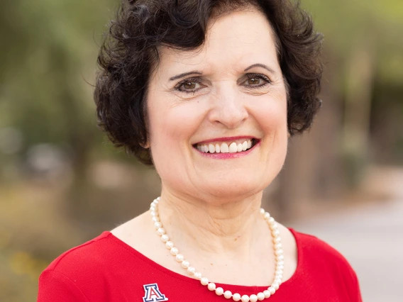 Headshot of woman looking at the camera and smiling wearing a red shirt, pearls and a U of A pin.