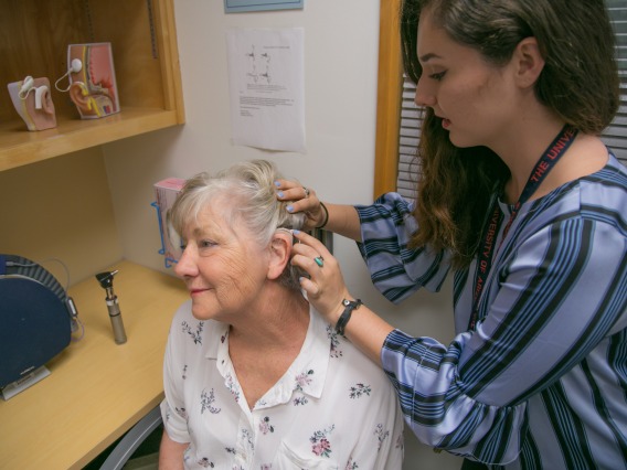 Graduate clinician fits audiology patient with hearing aid