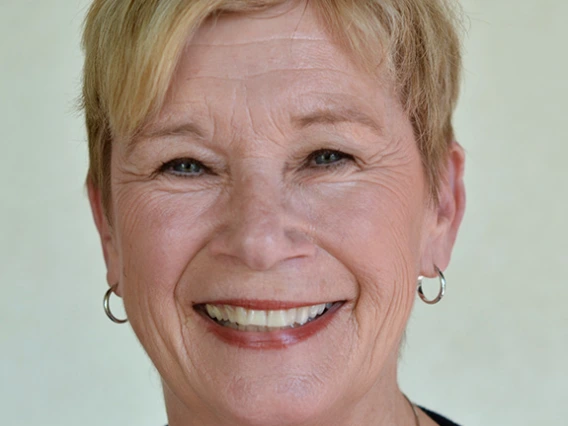 Headshot of woman with short blond hair wearing silver hoop earrings, necklace, and a black shirt smiling at the camera.