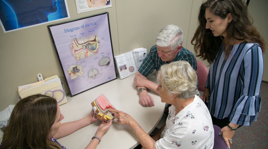 Four adults looking at model of cochlear implant