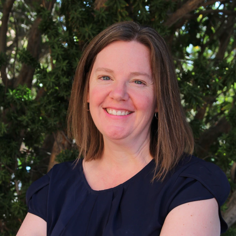 Image of woman smiling at camera with foliage in background