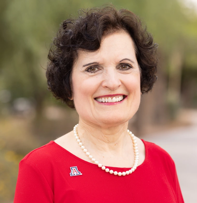 Headshot of woman looking at the camera and smiling wearing a red shirt, pearls and a U of A pin.