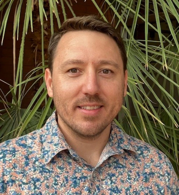 Headshot of man wearing light blue and pink floral shirt smiling at the camera