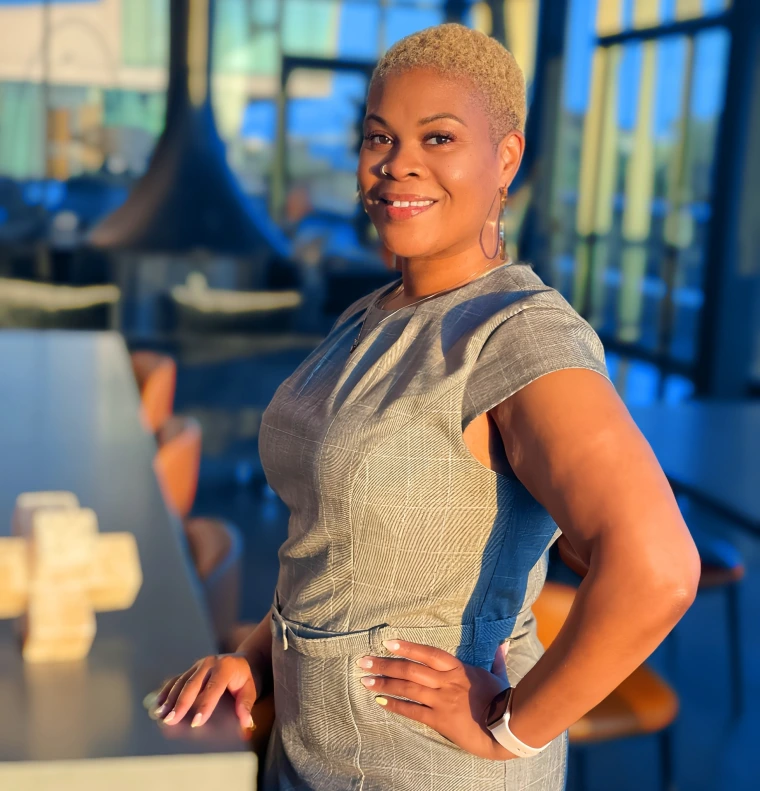 Image of a woman standing in front of a bay of windows smiling at the camera.