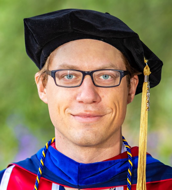 Image of man in graduation regalia smiling at camera