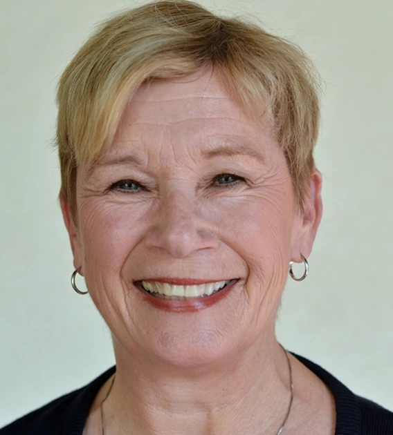 Headshot of woman with short blond hair wearing silver hoop earrings, necklace, and a black shirt smiling at the camera.