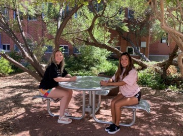 Two undergraduates sitting at the new table under the trees