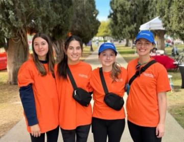 4 women in matching orange shirts pose at a park