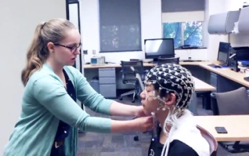 Dr. Kielar lab photo; student placing a brain scanner cap on another person